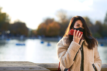 Beautiful woman with facemask sending a text message in a park