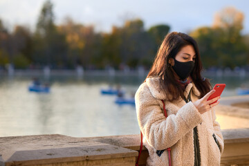Beautiful woman with facemask sending a text message in a park