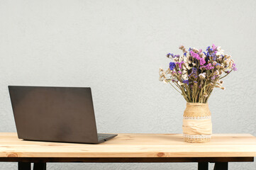 Open laptop and a vase of flowers on a wooden table.