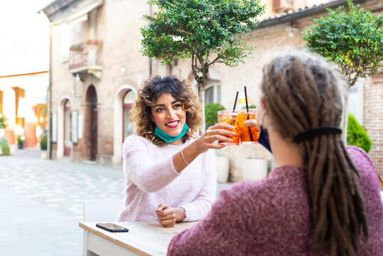 Happy Millenial Couple Wearing Protective Face Mask Having Fun Together At Bar Cafeteria. New Normal Lifestyle Concept With Young People On Positive Mood Drinking Cocktails On A Open Air Restaurant.