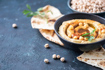 Hummus, chickpea dip, olive oil, raw beans, smoked paprika, pita on dark authentic background. Middle eastern, jewish cuisine or arabic dishes. Top view. Copy space. Vegan, vegetarian food concept