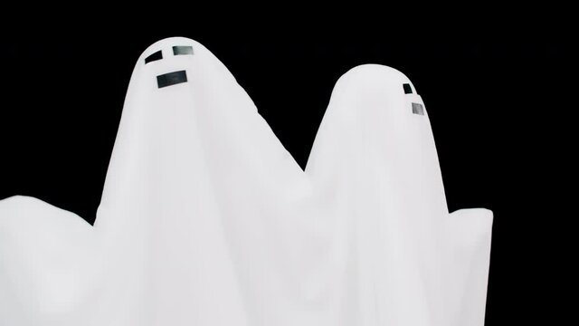 Two whiteghost at dark background horror . Halloween holiday, character costumes for terrible holiday. Couple white cast in sheet on black background.