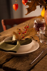 Autumn table setting, green napkin with dry oak leaf and rosehip branch on a plate, wooden table