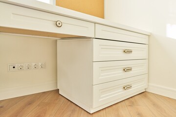 White wooden chest of drawers with vintage bronze handles under desk