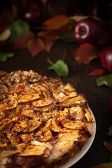 Delicious sweet pie with red apples, apple pie sprinkled with cocoa on a wooden background, rustic style, background of red leaves of grapes and ripe fruits