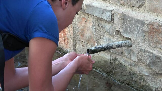 Fethiye, Turkey - 8th of November 2020: 4K Thirsty woman drinks natural spring water from fountain on the road
