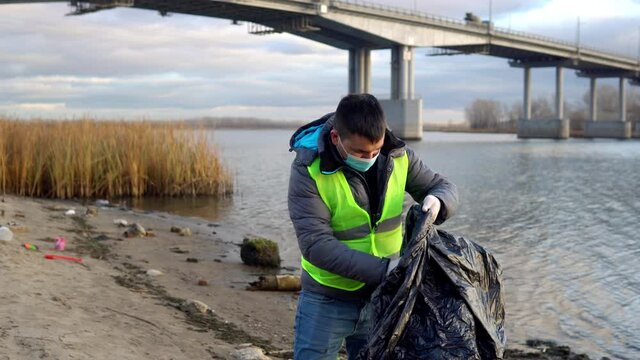 A volunteer on a city beach found a used condom and puts it in a garbage bag. Environmental pollution
