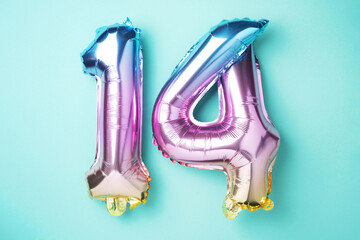 Creative layout. Rainbow foil balloon number, digit fourteen. Birthday greeting card with inscription 14. Anniversary concept. Top view. Stylish colored numeral on blue background. Numerical digit