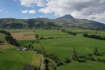 Obraz premium Aerial view of an agriculture landscape with many farms that have lush green meadows and mountains in the background