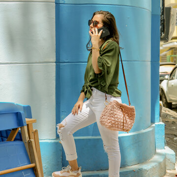 Mulher parada em uma esquina falando ao telefone e usando uma bolsa de crochê 