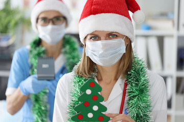 Two female doctors in protective medical masks and santa claus hats are smiling. Celebrating New Year and Christmas in hospitals near coronavirus pandemic concept