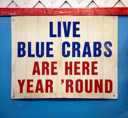 LIVE BLUE CRABS ARE HERE YEAR ROUND sign mounted on blue wall. Chesapeake Bay, Virginia.
