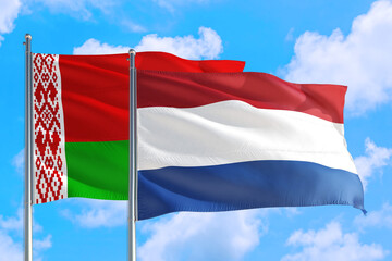 Fototapeta na wymiar Netherlands and Belarus national flag waving in the windy deep blue sky. Diplomacy and international relations concept.