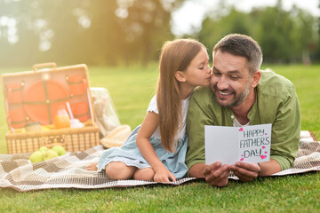 Happy father received handmade postcard from his daughter, little girl and her daddy having a picnic in the park on a warm day