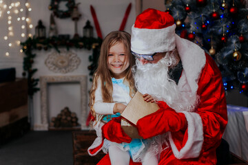 A child with Santa Claus open presents at the Christmas tree.