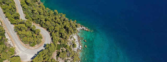 Aerial drone ultra wide top down panoramic photo of curvy snake road crossing through vegetated tropical forest by the sea