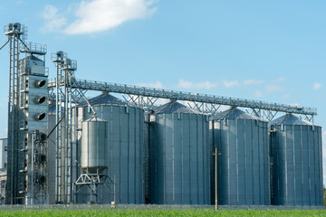 silver silos on agro manufacturing plant for processing drying cleaning and storage of agricultural products, flour, cereals and grain. Large iron barrels of grain. Granary elevator