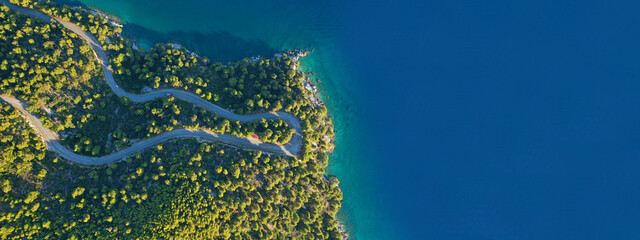 Aerial drone ultra wide top down panoramic photo of curvy snake road crossing through vegetated tropical forest by the sea