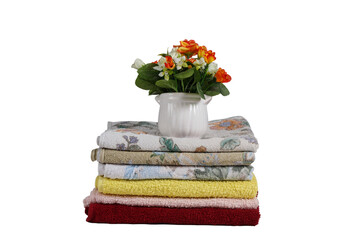 a stack of towels of different colors and a bouquet of flowers in a vase isolated on a white background.