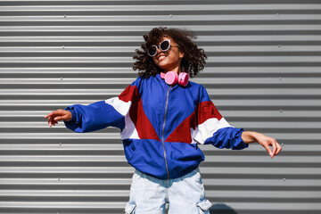 Cool black girl with curly hair, glasses, 90s, 80s, retro hip hop style, dancing against a metal...