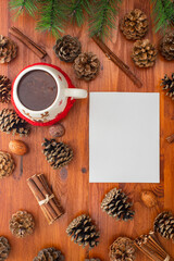Christmas background. pine cones and green needles. plain white sheet of paper. cup of hot cocoa. wood table.