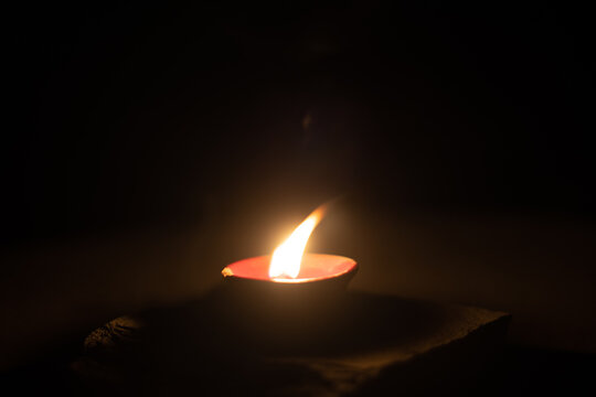 dark minimalistic image showing a diya oil lamp filled with oil or ghee and burning a cotton wick to produce a flame, its a popular religious item and decoration item on the hindu festival of diwali
