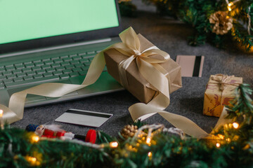 Christmas shopping online with a credit card for the holiday. Laptop with gifts on the table next to fir branches and a garland of lights