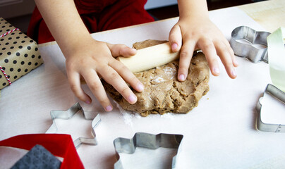 Child's hands rolling out dough for christmas cookies. Little mom's assistant, Preparing for the...
