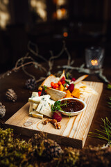 Cheese plate served with grapes, jam, figs, crackers and nuts on a wooden background with natural decorations