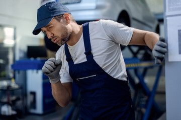 Auto mechanic coughing while working at repair shop.