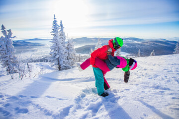 Young woman skier hugs snowboarder guy and throws snow. Concept family active winter vacations