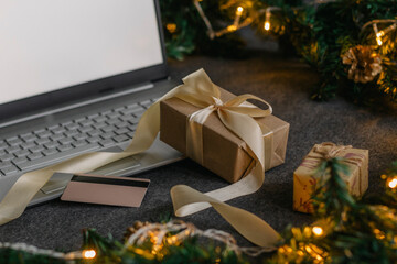 Christmas shopping online with a credit card for the holiday. Laptop with gifts on the table next to fir branches and a garland of lights