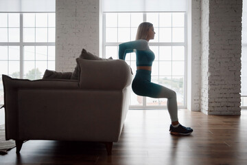 Slim sporty girl uses sofa to stretch her legs at home. Concept Lifestyle sports for pandemic