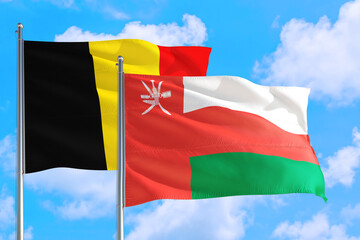 Oman and Belgium national flag waving in the windy deep blue sky. Diplomacy and international relations concept.