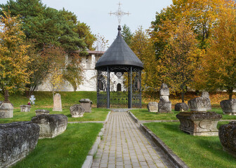 Churchyard with ancient tombstones and beautiful metal pergola in the Holy Dormition monastery, Staritsa, Tver region, Russia. Scenic view of the old cemetery in the time of golden autumn