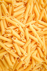 Uncooked penne pasta close up, background. Vertical photo