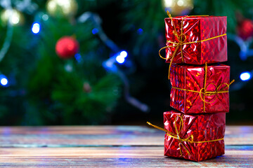 Red gift boxes on a wooden table against the background of defocus from lights with copy space. New Year card