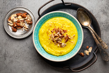 Traditional Indian dish Kheer, sweet rice milk pudding with almonds and saffron in blue ceramic bowl with spoons on stone rustic background, top view. Dessert meal of Indian cuisine