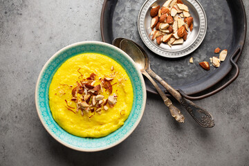 Traditional Indian dish Kheer, sweet rice milk pudding with almonds and saffron in blue ceramic bowl with spoons on stone rustic background, top view. Dessert meal of Indian cuisine
