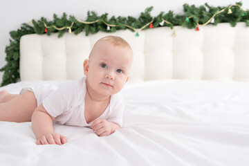 blonde baby boy lying on white bedding at home with Christmas decorations.