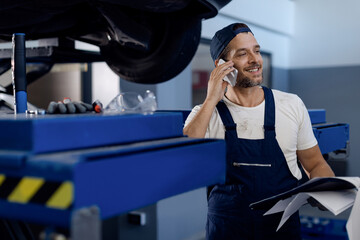 Happy mechanic talking on the phone while working at auto repair shop.