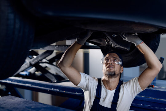 Mid Adult Mechanic Repairing Undercarriage Of A Car In Auto Repair Shop.