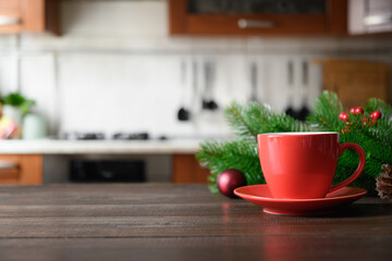 Wooden tabletop with red cup of coffee and blurred Christmas kitchen.