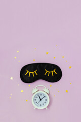 Black sleep mask, alarm clock and starry confetti on pastel background. Waking up concept. Vertical flatlay, top view