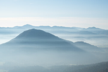 mystical and romantic mountain scenery with hilltops softly peaking out of white clouds. Fog flowing through the valleys. Layers of mountains in a beautiful landscape with the alps in the background 