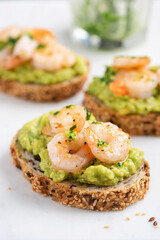 Bruschetta with avocado cream and shrimps on white marble background, closeup view. Appetizer or snack avocado toasts with prawn