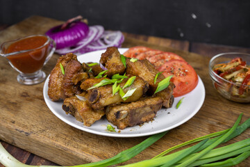 Grilled fat pork ribs on a bone served on a plate with vegetables. Roasted barbeque meat on dark background.