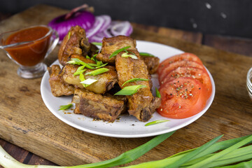 Grilled fat pork ribs on a bone served on a plate with vegetables. Roasted barbeque meat on dark background.