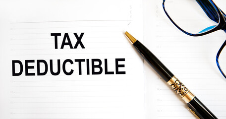 In the notebook the text OF TAX DEDUCTIBLE, next to the pen, glasses.