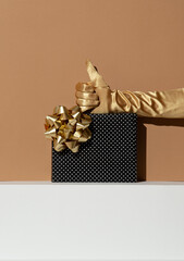 Hand in golden gloves holding gift box. Minimal still life design. Holiday,christmas, birthday concept. Thumbs up idea for present